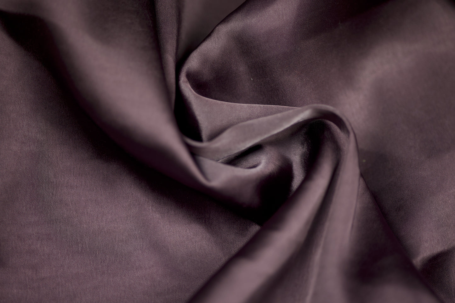 Nahaufnahme eines luxuriösen Satinstoffs in pflaumenfarbener Optik mit seidigem Glanz und weichem Faltenwurf – ideal für elegante Kleidung und kreative Projekte.