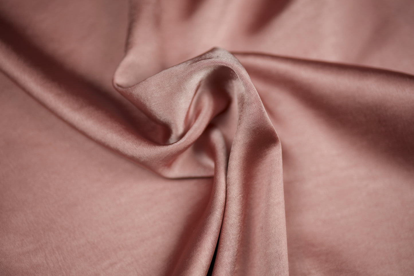Nahaufnahme eines luxuriösen Satinstoffs in zartem Roséton mit seidigem Schimmer und dekorativer Faltenlegung – ideal für romantische Näharbeiten.