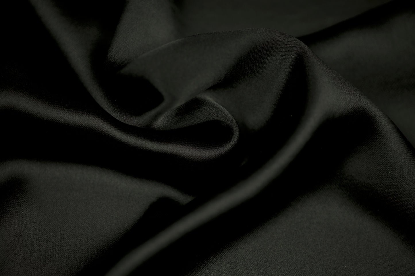 Nahaufnahme eines luxuriösen Satinstoffs in elegantem Schwarz mit weichem Faltenwurf und seidig glänzender Oberfläche.