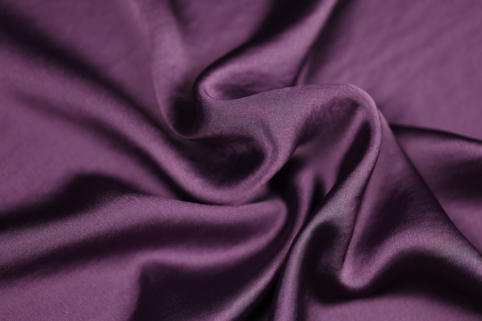 Nahaufnahme eines luxuriösen Satinstoffs in tiefem Aubergine mit edlem Glanz und weicher Faltenstruktur – perfekt für elegante Mode und kreative Projekte