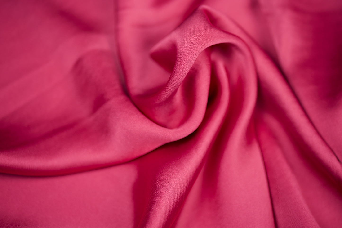 Nahaufnahme eines luxuriösen Satinstoffs in intensivem Himbeerrosa mit elegantem Glanz und dekorativer Faltenstruktur – ideal für auffällige Nähprojekte
