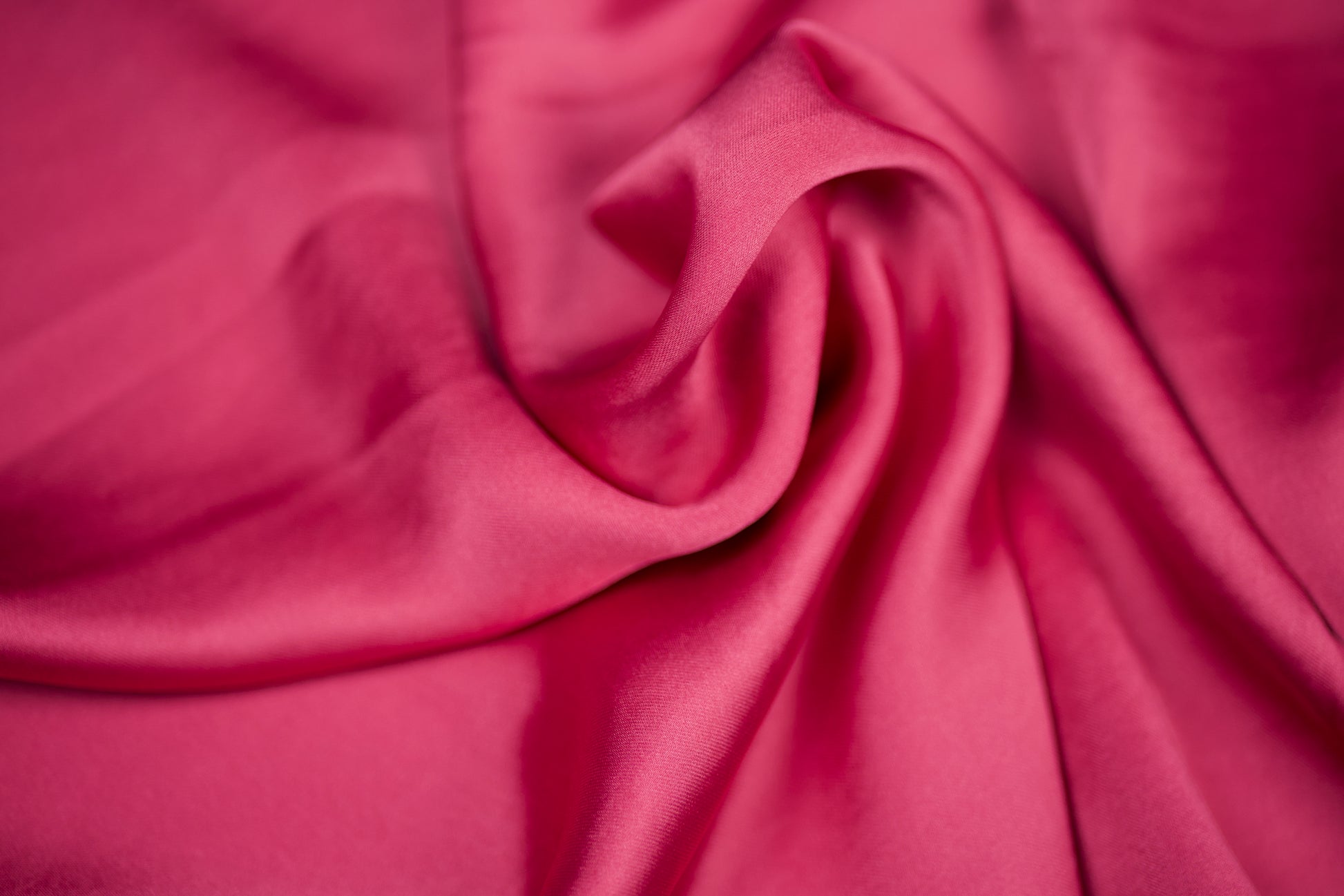 Nahaufnahme eines luxuriösen Satinstoffs in intensivem Himbeerrosa mit elegantem Glanz und dekorativer Faltenstruktur – ideal für auffällige Nähprojekte