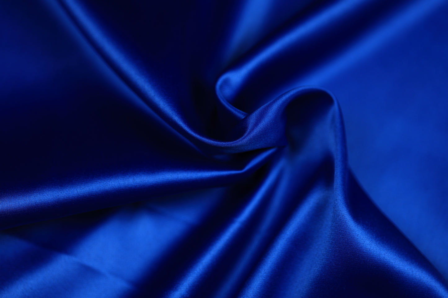 Nahaufnahme eines luxuriösen Satinstoffs in kräftigem Königsblau mit geschwungener Drapierung und intensivem Glanz – perfekt für festliche Kleidung und elegante Dekoration