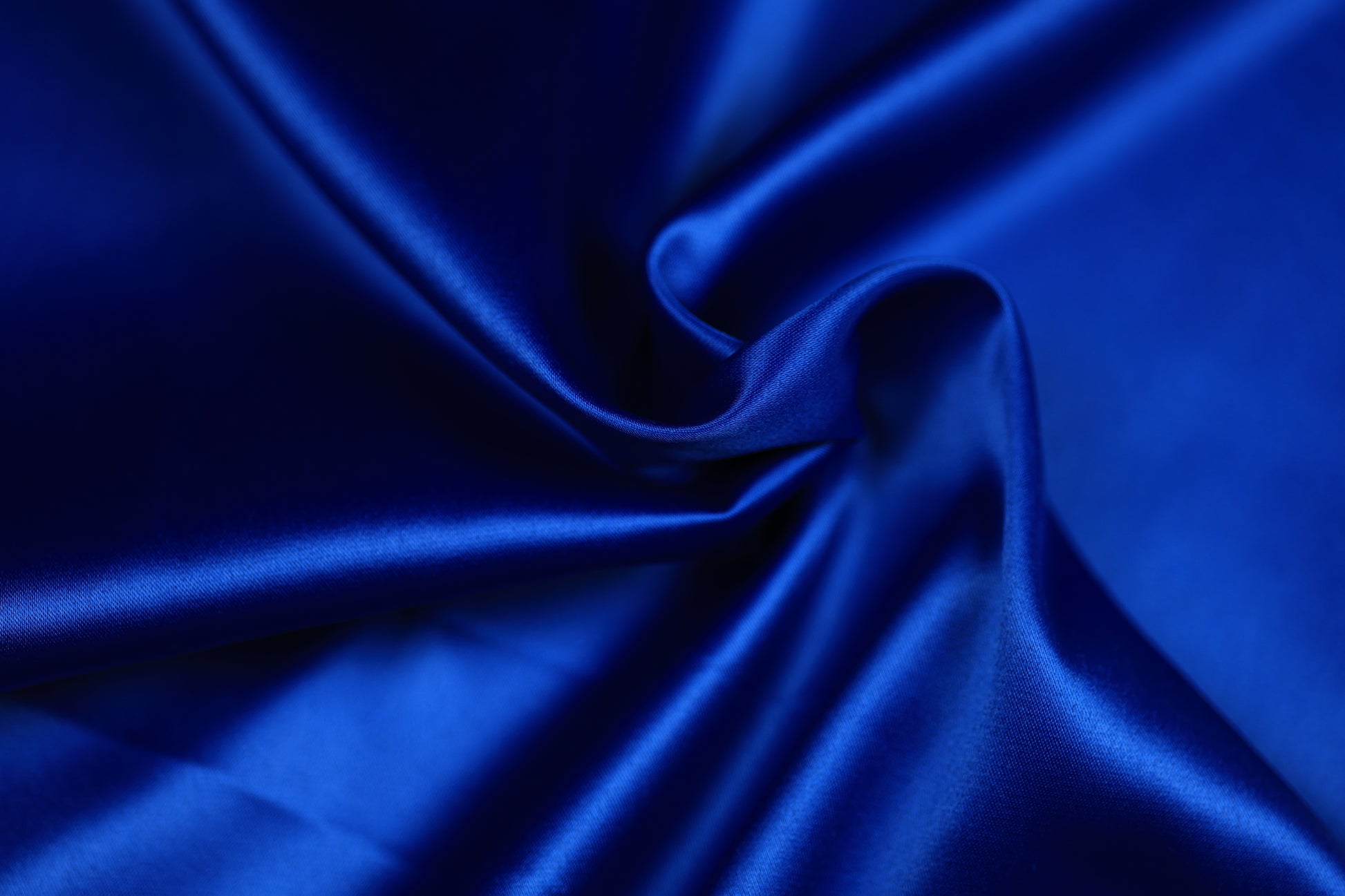 Nahaufnahme eines luxuriösen Satinstoffs in kräftigem Königsblau mit geschwungener Drapierung und intensivem Glanz – perfekt für festliche Kleidung und elegante Dekoration