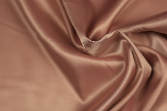 Nahaufnahme eines weich fallenden Satinstoffs in sanftem Rosé-Nude mit feinem Glanz und eleganter Faltenstruktur – perfekt für festliche Kleidung und stilvolle Deko