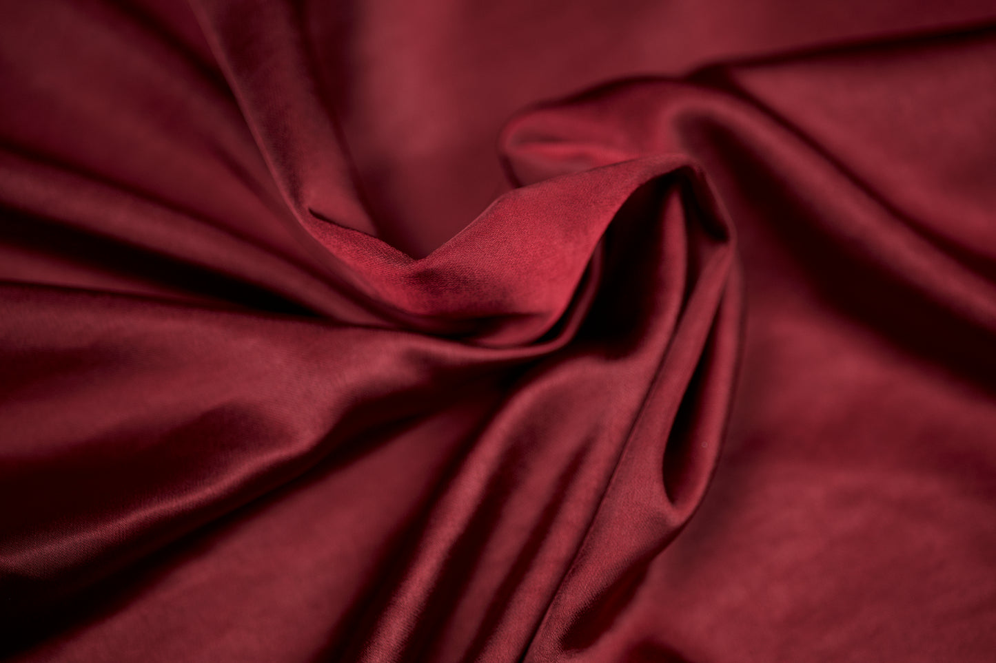 Nahaufnahme eines luxuriösen Satinstoffs in kräftigem Bordeaux mit seidig glänzender Oberfläche und weichem Faltenwurf – ideal für Abendmode und Dekoration