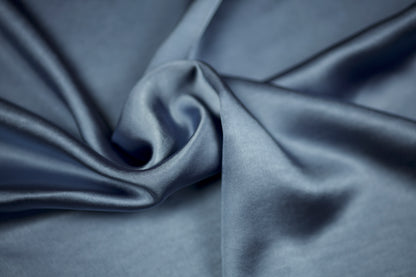 Luxuriöser Satinstoff in Taubenblau mit sanftem Glanz und geschwungener Drapierung – detailreiche Nahaufnahme